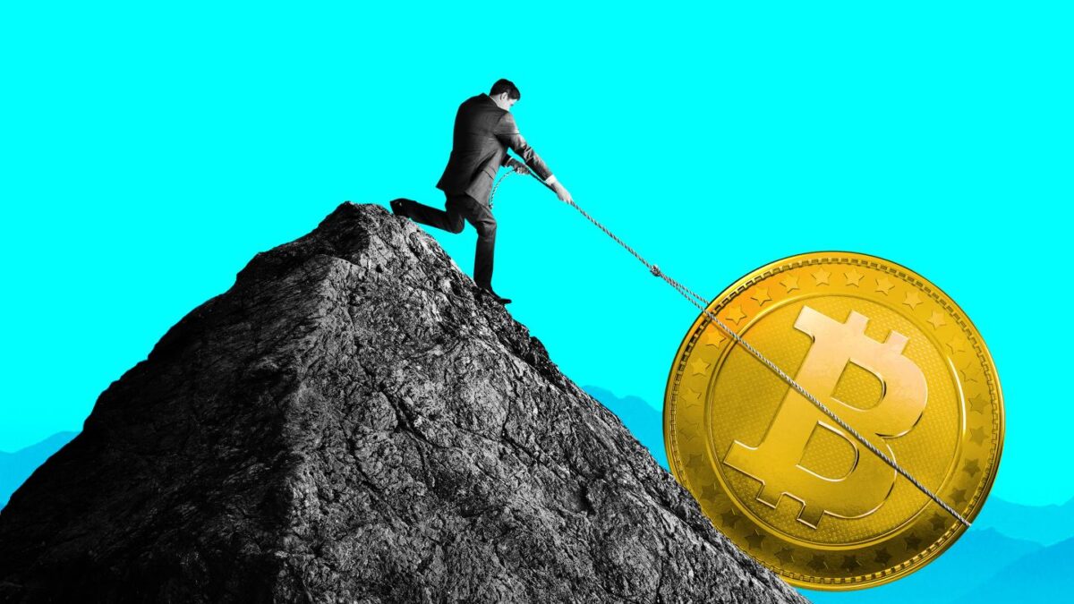 A man tries to pull a coin with the Bitcoin logo back up a mountain.