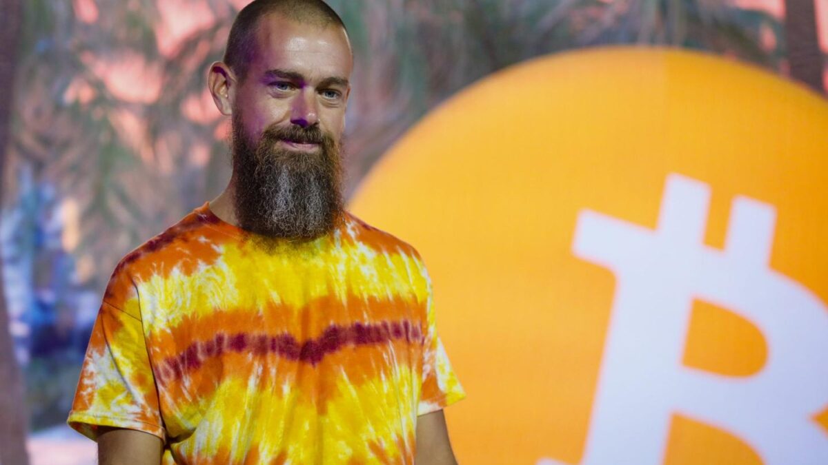 Jack Dorsey stands on stage next to a Bitcoin logo.