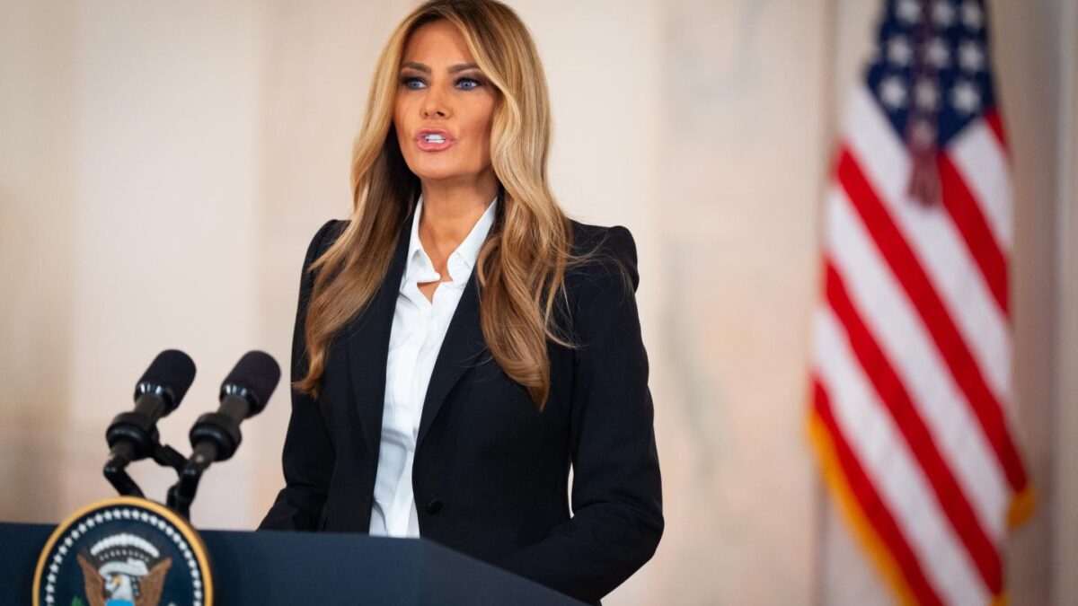 Melania Trump standing behind a podium with American flag behind her