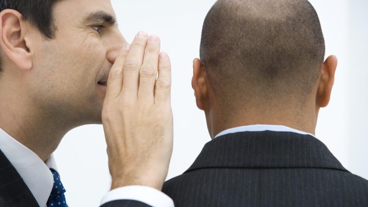 A man in a suit whispering to another man in a suit.