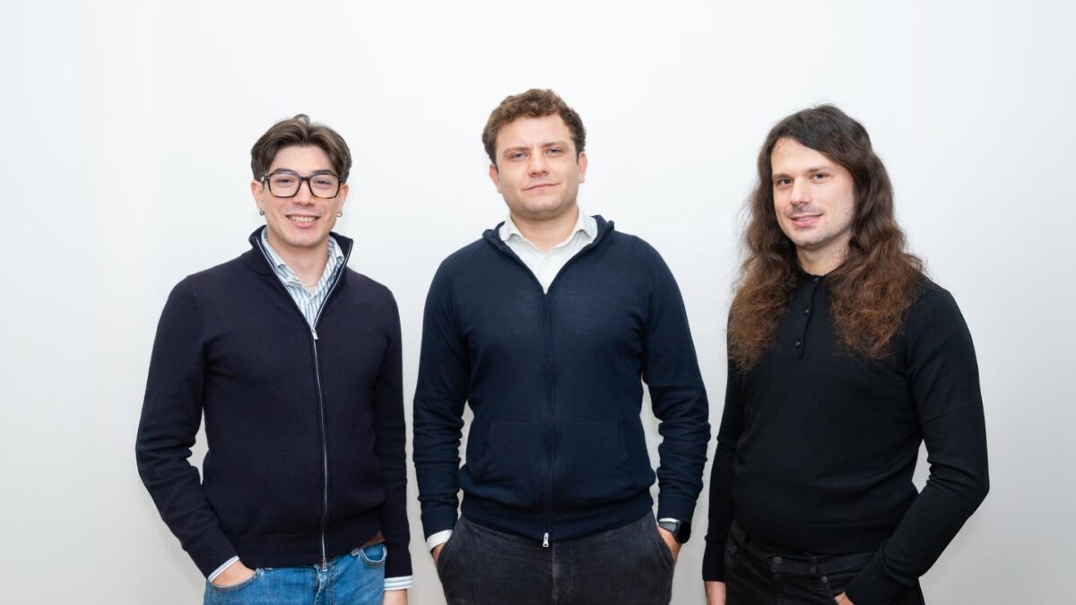 Three men stand in front a white backdrop.