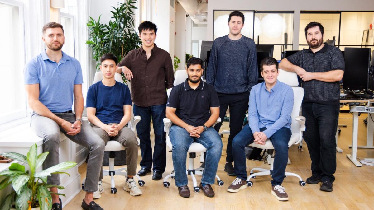 Seven men stand and sit in a modern-looking office