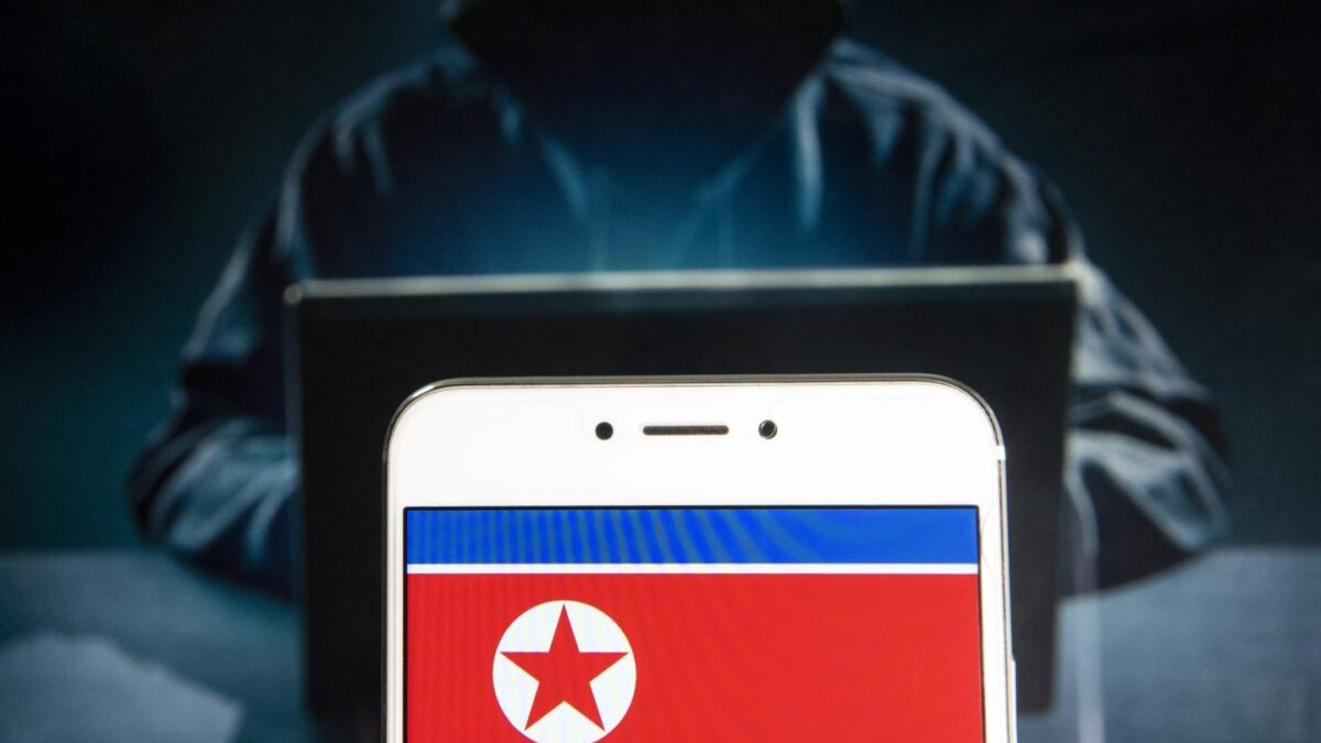 Photo illustration of the North Korean flag seen on a screen with the image of a hacker behind it