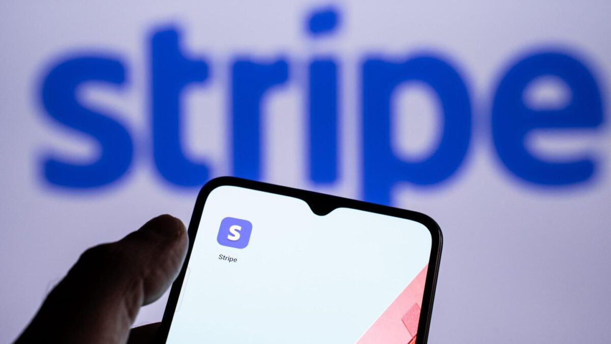 Someone holds a phone with the Stripe app in front of a screen displaying the Stripe logo